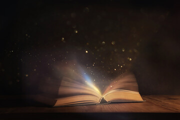 Magical image of open antique book over wooden table with glitter lights - Powered by Adobe