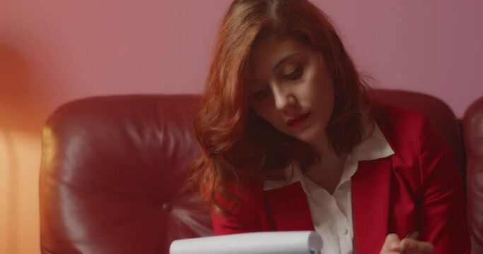 Giovane ragazza italiana scrive appunti di business su carta mentre &egrave; seduta sul divano in ufficio