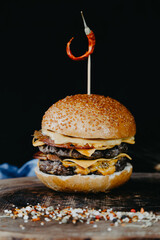 Double big hamburger on wooden plate with small grains of spice on black background