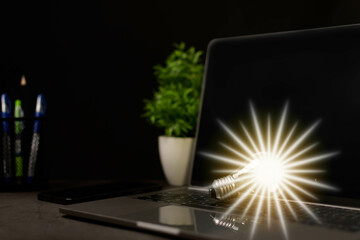 Close-up. A bright light bulb on a laptop. Concept of start-up that drives economy, finance, banking, real estate. Bright lights give hope to businessmen both small and large. Blurred black background
