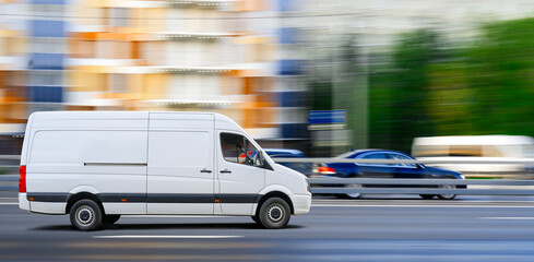 Fototapeta na wymiar White van drives on city traffic on cityscape background.