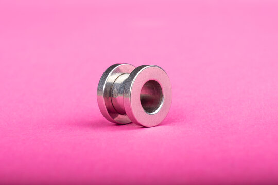 Piercing, Silver Ear Tunnel On Pink Background Close-up.