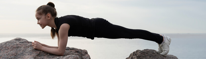 Girl gymnast performs various acrobatic exercises on stones against the background of the sea. Photo series.