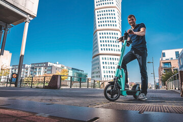 Young man riding an electric scooter down the streets in Malmo. Ecological transportation concept. 