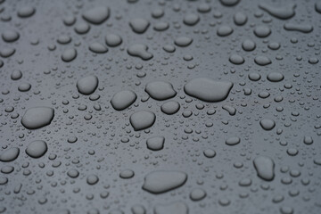 Closeup of raindrops on black hood of car background