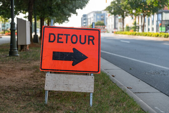 Orange and black detour sign with bold arrow on a city street