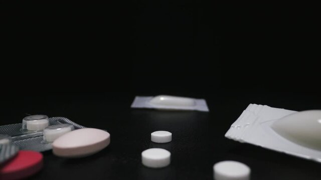 CU, macro: motion from suppository in pack above different scattered colorful drugs to cure virus lying on dark surface extreme close view