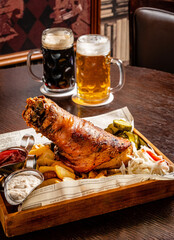 Traditional gourmet german snack of roasted potatoes, grilled pork ribs with fried vegetables, shank and beer in a pan on a grill panel.