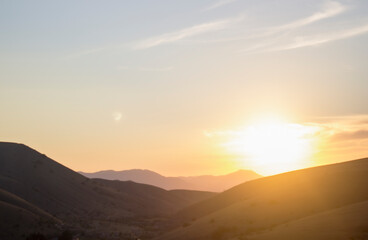 A bright sunset against the backdrop of green mountains and khoms.