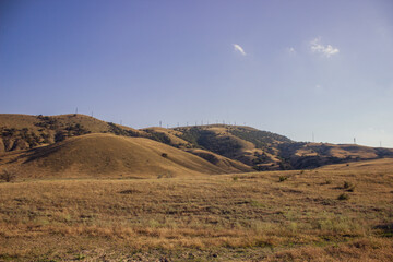 Windmills on a green hill against a background of blue sky and fields.