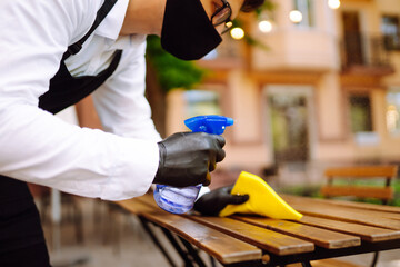 Disinfecting to prevent COVID-19. Waiter cleaning the table with Disinfectant Spray in a restaurant wearing protective medical mask and gloves.