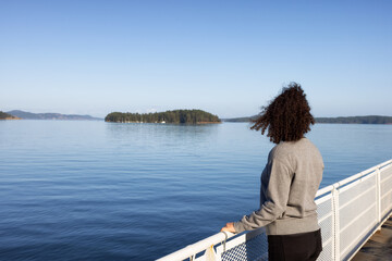 Fototapeta premium White Caucasian Adult Woman watching the Canadian Nature Scenery from a ferry boat. West Coast of Pacific Ocean. Vancouver Island, British Columbia, Canada.