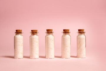 Pink Himalayan salt in glass bottles. Little bottles with cork stopper. Pink background.