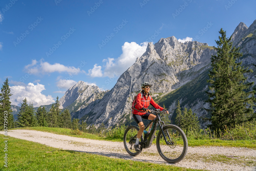 Wall mural beautiful active senior woman with electric mountainbike in the spectacular mountains of raintal val