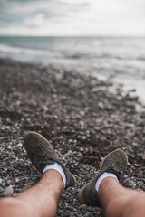 Male feet in the dark green sneakers on black pebbles on the beach in Batumi, Georgia. High quality photo