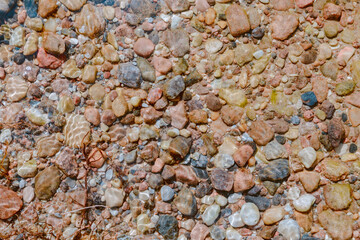 Multicolored small pebbles at the bottom of the lake under clear water