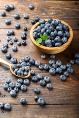 Freshly picked blueberries in a wooden bowl and spoon. Berries are scattered on a wooden table. Healthy berry, organic food, antioxidant, vitamin