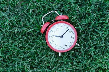 Red classic alarm clock lying on green grass closeup