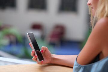 Young woman holding mobile phone in her hands and looking at screen closeup