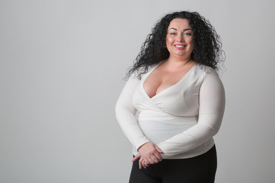 Plus size woman with deep cleavage and big breast posing in studio with happy toothy smile. Overweight female model with curly dark hair looking in camera 