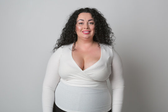 Overweight young woman with big breast wearing white shirt with deep cleavage posing in studio with happy smile