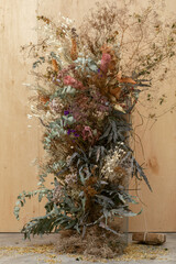 Large floral arrangement bouquet of dried flowers on the background of a wood wall and cement floor. The concept of inspiration, congratulations, autumn season, studio flower decoration.