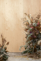 Large floral arrangement bouquet of dried flowers on the background of a wood wall and cement floor. The concept of inspiration, congratulations, autumn season, studio flower decoration.