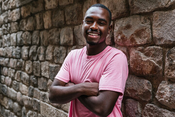 horizontal portrait of an afro american young man. He is looking at camera with a stone wall on the background