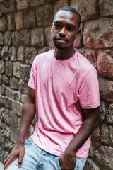 Fototapeta premium vertical portrait of an african young man. He is looking at camera with a stone wall on the background