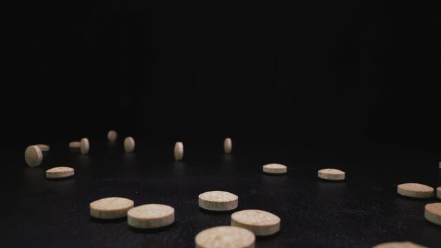 CU, macro shot: numerous light brown antiviral pills fall down to pile and roll around on black surface against dark background zoom out extreme close view