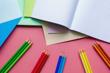 School and hobby concepts. Colored paper sheets, colored pencils and notebook on pink paper background.  Free space for text