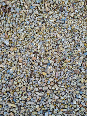 Multicolored small stones are evenly scattered and create a beautiful small stone background. Daylight. View from above