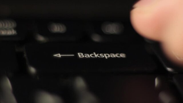 The finger presses the backspace button on the keyboard. Close-up.