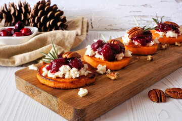 Roasted autumn sweet potato crostini appetizers with cheese, cranberries and pecans on a wood...
