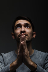 Headshot of serious confident young man praying in dark room. Lit from above and looking up