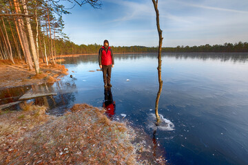 the man stands on The first transparent ice on the northern lake in the forest in late autumn in November, First frosts