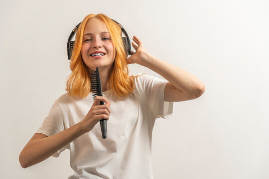 portrait of a teenage girl with red hair and in a white T-shirt singing in a hairbrush on a light background