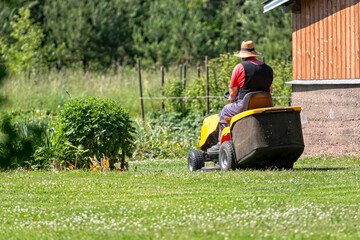 a senior man with a lawn mower mows the grass in the yard of country house