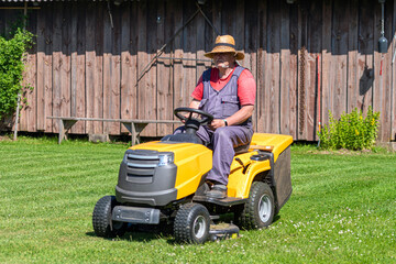 a senior male with a lawn mower mows the grass in the yard of country house