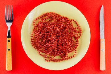 Christmas cutlery and beads. Red Christmas beads on a green plate. Christmas dinner concept. Top view