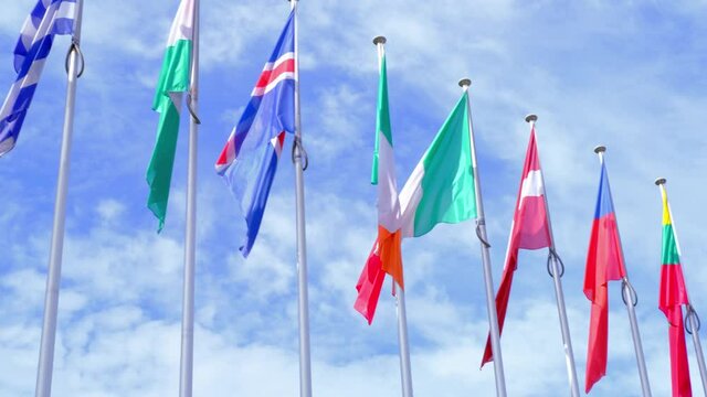 national flags of Europe and other countries on satin flutter in wind in blue sky near building of European Parliament, state symbols, concept of international cooperation, global business