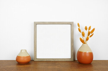 Mock up wood frame with autumn branches and home decor on a wooden shelf. Fall concept. Square frame against a white wall.