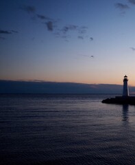 Lighthouse at sunset or twilight. Soft hint of orange color in clouds above the horizon and small lighthouse almost in silhouette at right.  Great South Bay, Long Island, New York State.  Vertical.