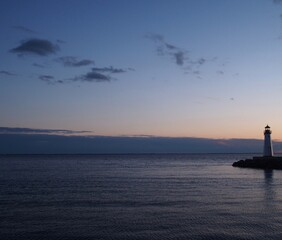 Lighthouse at sunset. Soft pastel colors of twilight, clouds above the horizon, and small lighthouse almost in silhouette at right. Long Island, New York State.  With copy space.  Horizontal.