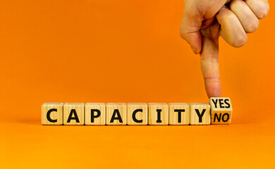 Capacity symbol. Businessman turns a wooden cube and change words 'capacity no' to 'capacity yes'. Beautiful orange background. Business and capacity concept, copy space.