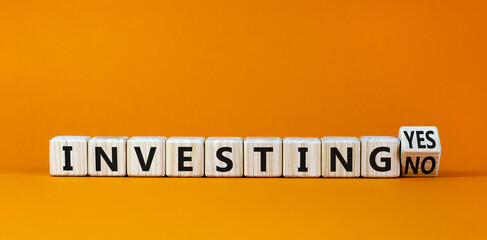 Investing yes or no symbol. Turned a wooden cube and changed words 'investing no' to 'investing yes'. Beautiful orange background. Business and investing yes or no concept, copy space.