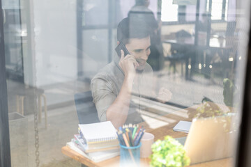 Photo through the office glass young businessman talking on the phone, he runs a startup company founded with partners, he is a young and energetic executive and grows the company's earnings.