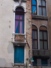 Fototapeta na wymiar Venice, Italy - Narrow windows of two neighboring buildings, hint of purple curtains, damaged walls, seen from back alley