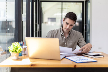 Fototapeta premium Young businessman sitting in the office at his company, he is checking the correctness of company financial documents, young businessman running a startup business is constantly profitable.