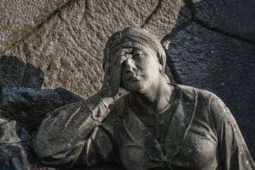 A sculpture of sad woman in grief. Virgin Mary stone statue (faith, suffering, death concept)